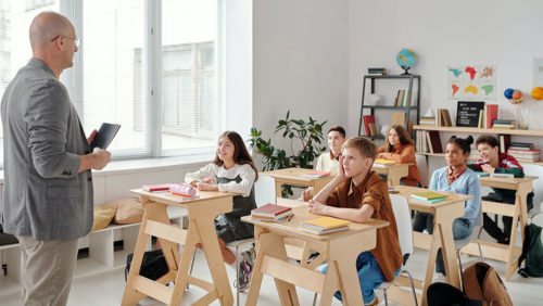 uczniowie siedzący przy biurkach w klasie szkolnej słuchający nauczyciela