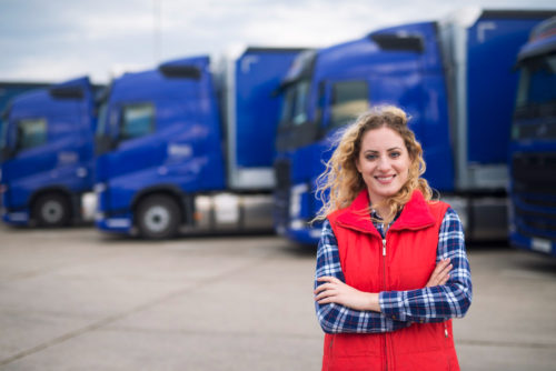 kobieta w czerwonej kamizelce na tle niebieskich ciężarówek
