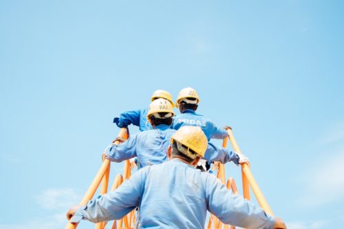 inżynierowie w niebieskich uniformach i żółtych kaskach wspinający się po żółtych schodach