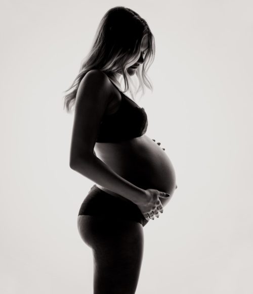 czarno białe zdjęcie kobiety w ciąży stojącej bokiem do obiektywu