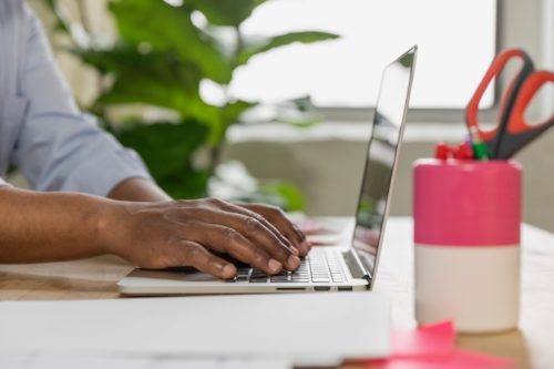 czarnoskóry mężczyzna pracujący przy biurku na laptopie, obok różowy pojemnik na przybory biurowe