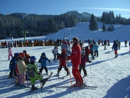nauka jazdy na nartach, mężczyzna w czerwonym kombinezonie narciarskim, gromadka dzieci pod opieką instruktora