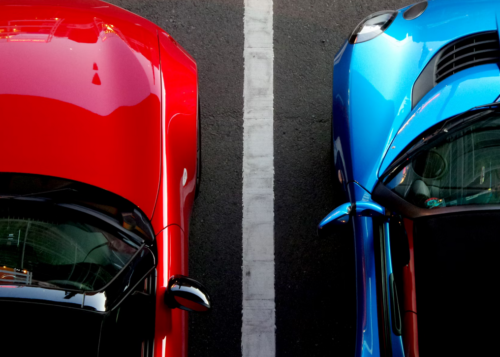 dwa samochody zaparkowane obok siebie, czerwona i niebieska karoseria