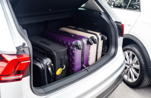 biały samochód z otwartą klapą bagażnika, bagażnik wypełniony walizkami w różnych kolorach