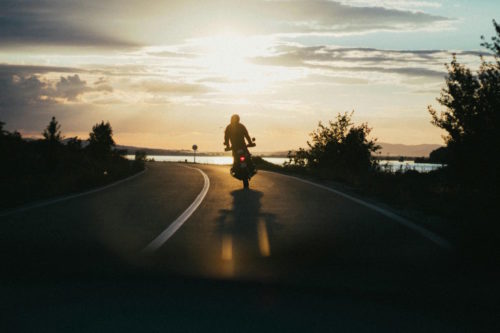 widok na drogę o zachodzie słońca wzdłuż lini brzegowej po której jedzie motocyklista