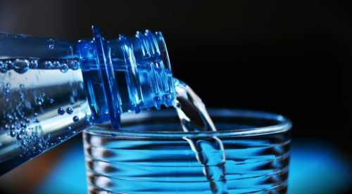 niebieska butelka z której jest nalewana woda do szklanki