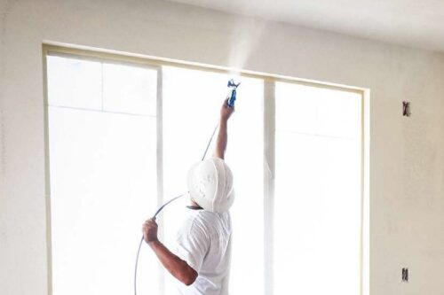mężczyzna maluje ściany i sufit metodą natryskową