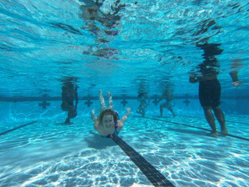 kobieta pływająca pod wodą w basenie pełnym ludzi