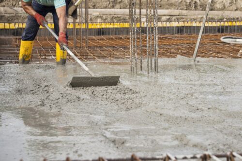 murarz w pracy na placu budowy podczas układania betonu w celu zbudowania fundamentów domu